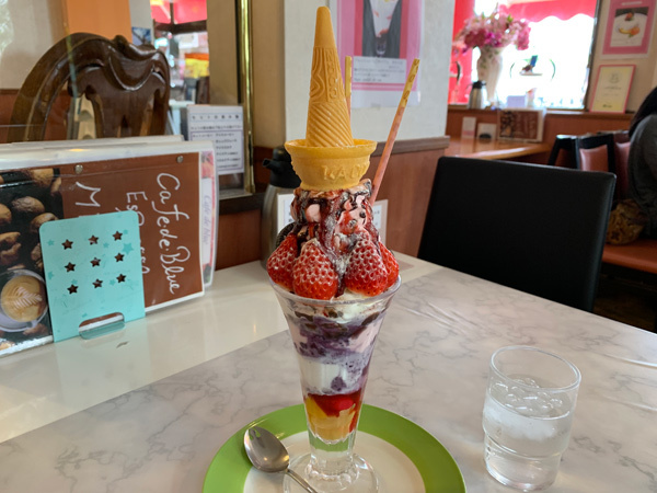 サポーターお薦め「カフェド ブルー」を訪問。お店の人のお薦め、いま旬のいちごパフェを注文。普通サイズでも大きい。しかもパフェの種類が数え切れないほど、たくさんある。